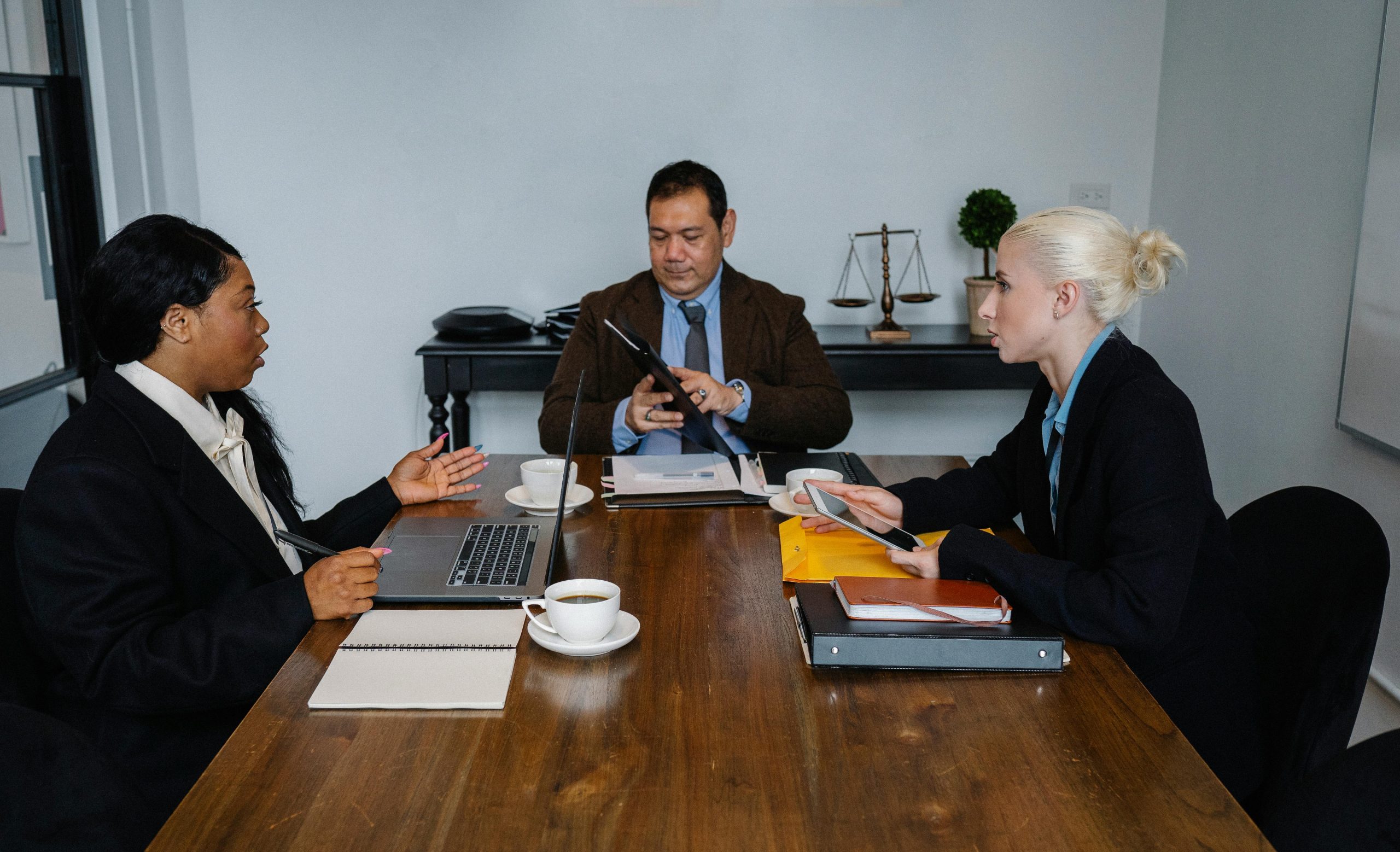 A diverse group of business professionals meeting indoors with laptops and documents.